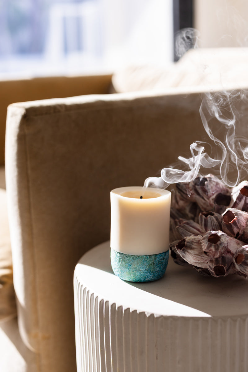 Candle with blue base and white holder on a radiator with steam rising.